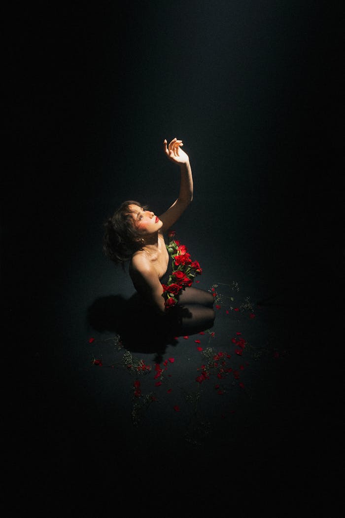 An evocative portrait of a woman enveloped in roses, reaching towards light, creating a dramatic ambiance.